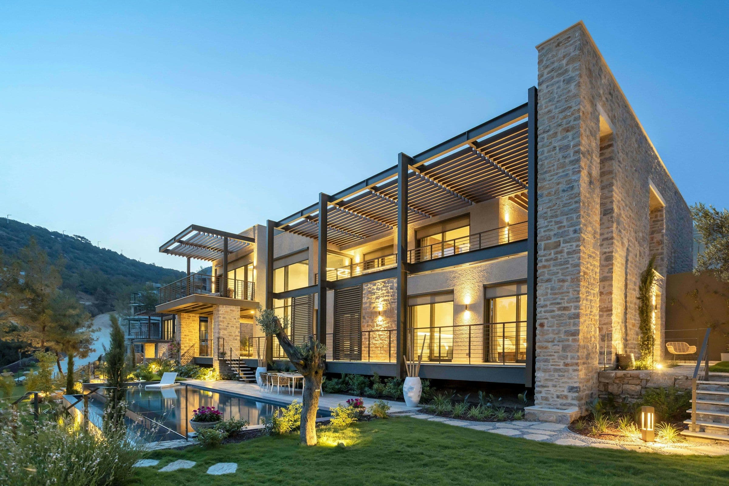 Modern villa at dusk with a lit garden, lawn and pool landscaped by Oasis Growers & Landscapers